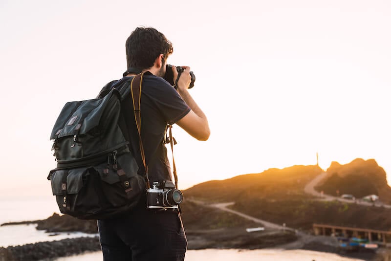 Man with Vintage Camera and a Travel Backpack at Sunset